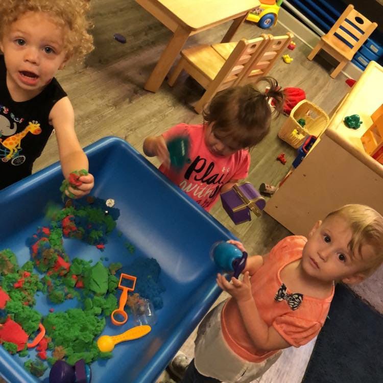 Three children playing with kinetic sand in a blue bin