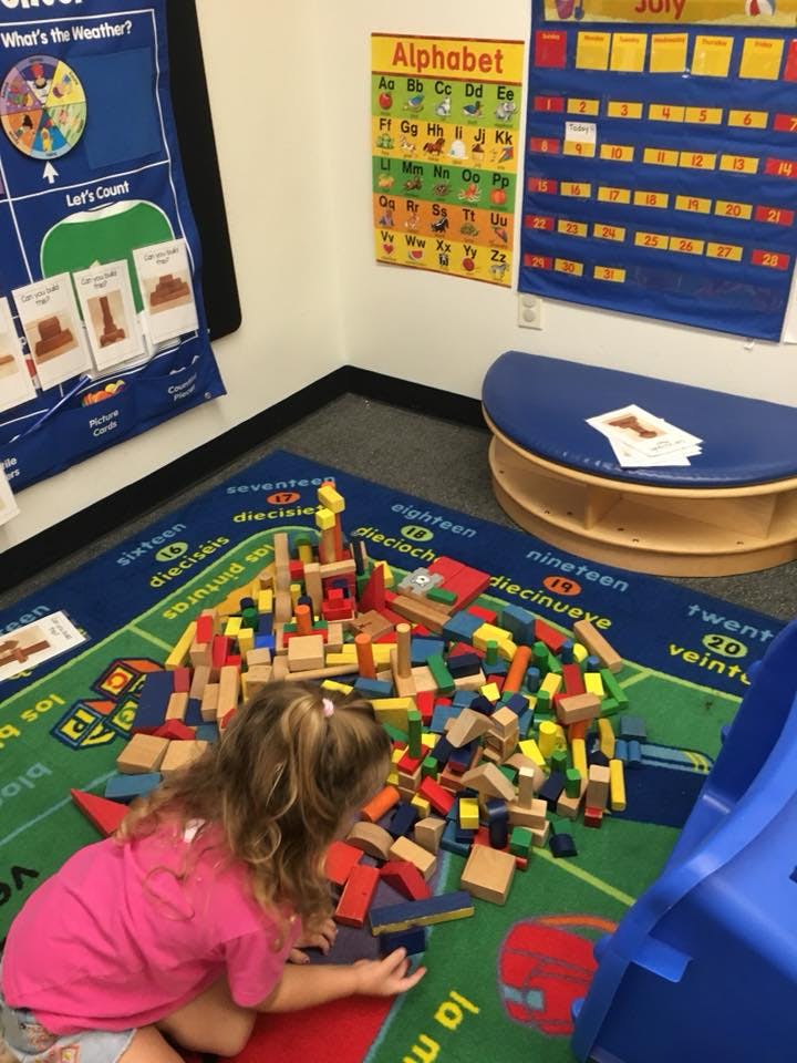 Child playing with colorful building blocks on a rug in a classroom