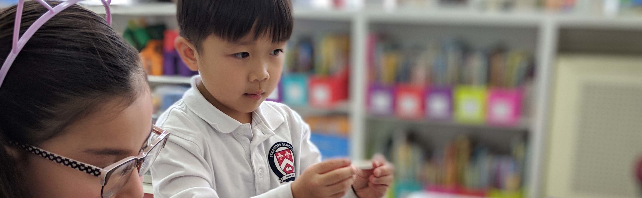Child in a white uniform holding a small white object with another child nearby
