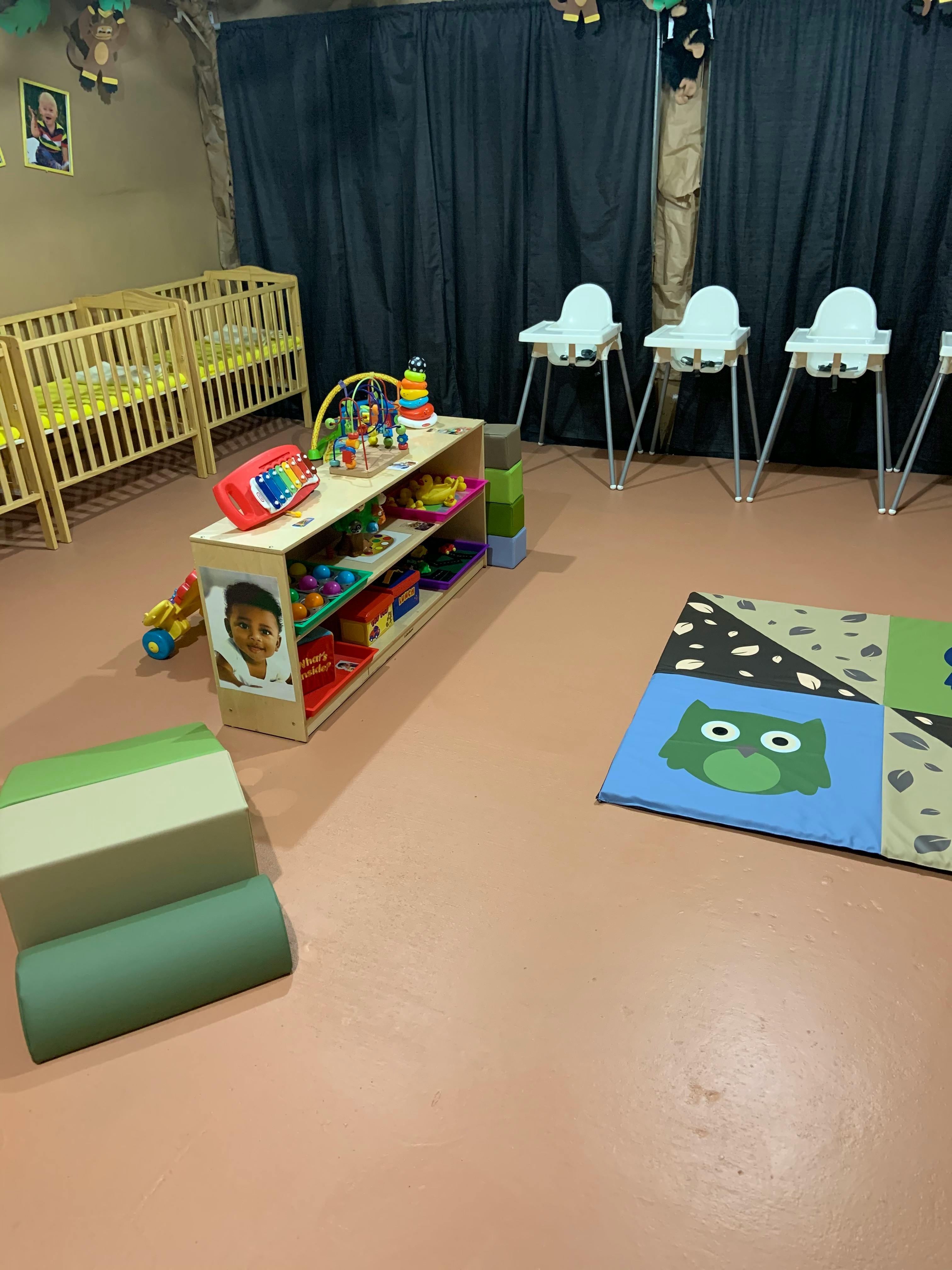 Nursery room with cribs, high chairs, toy shelf, and play mat