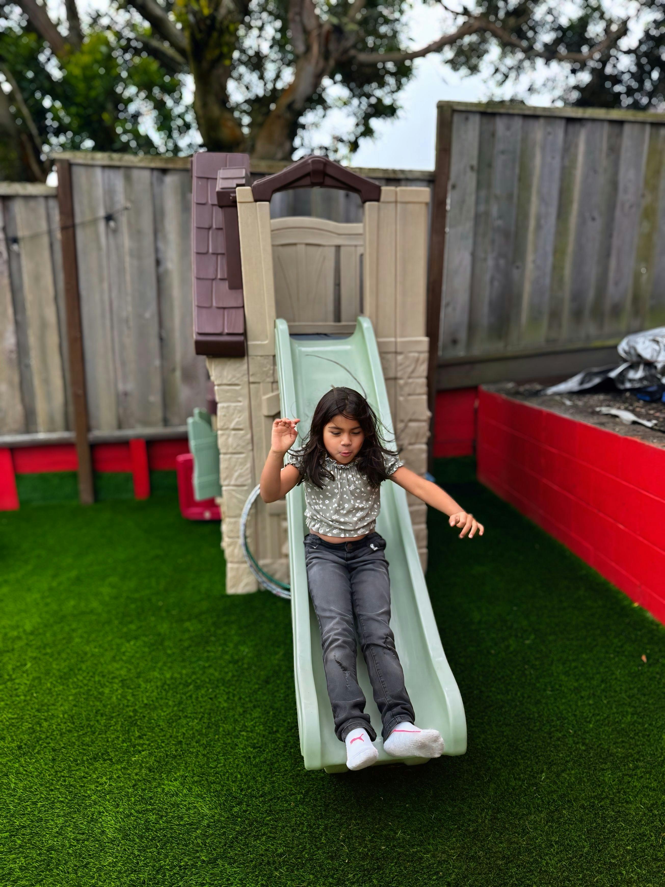Child sliding down a small playground slide on artificial grass