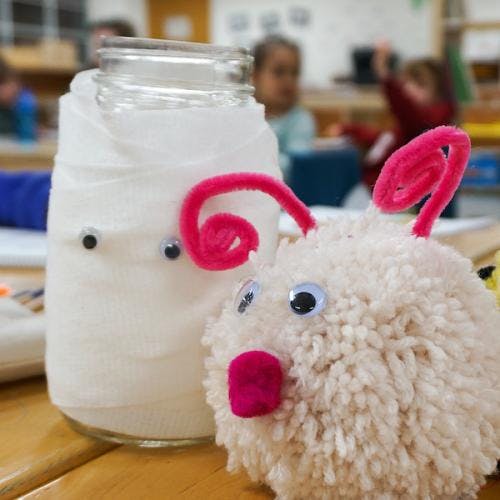 Mummy jar craft with googly eyes next to a pom-pom craft monster with antennae
