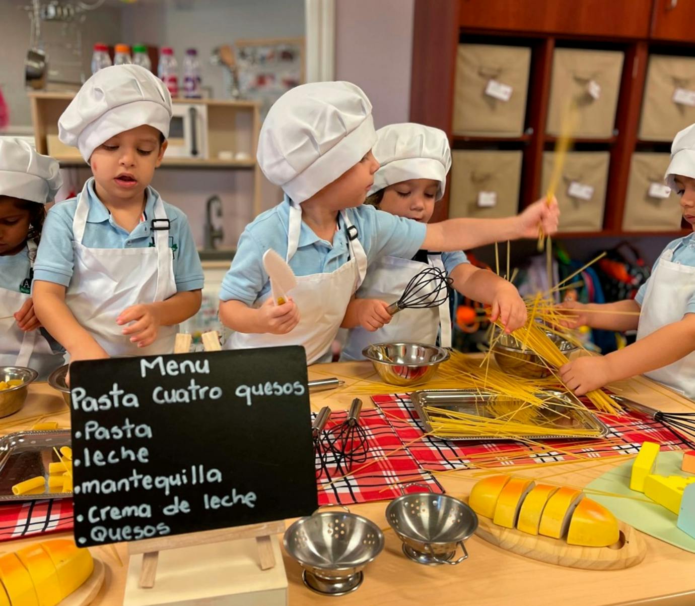 Children in chef hats and aprons preparing pasta at a table