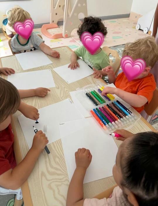 Group of children sitting at a table drawing with markers on paper