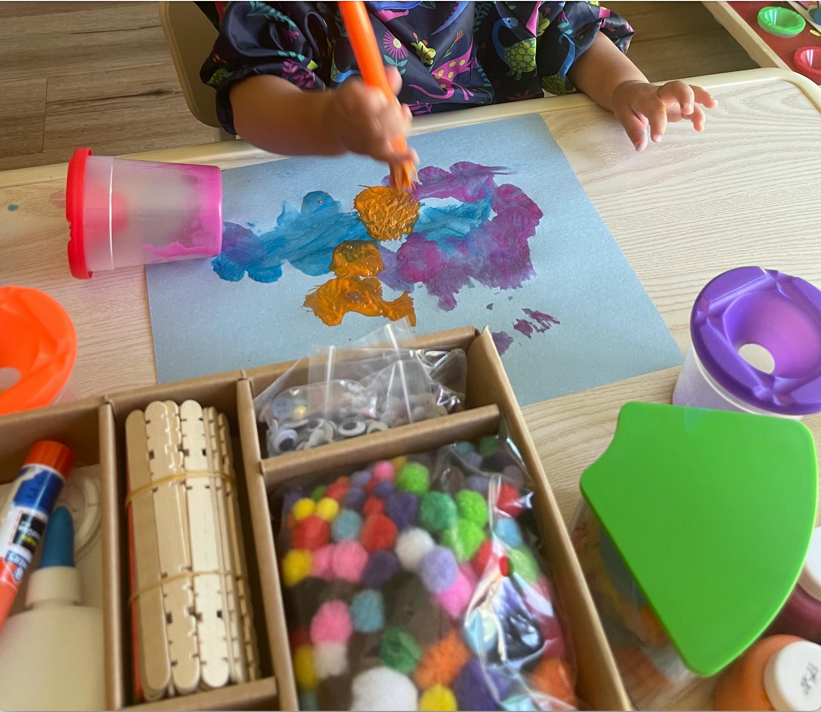 Child painting on paper with craft supplies on a table