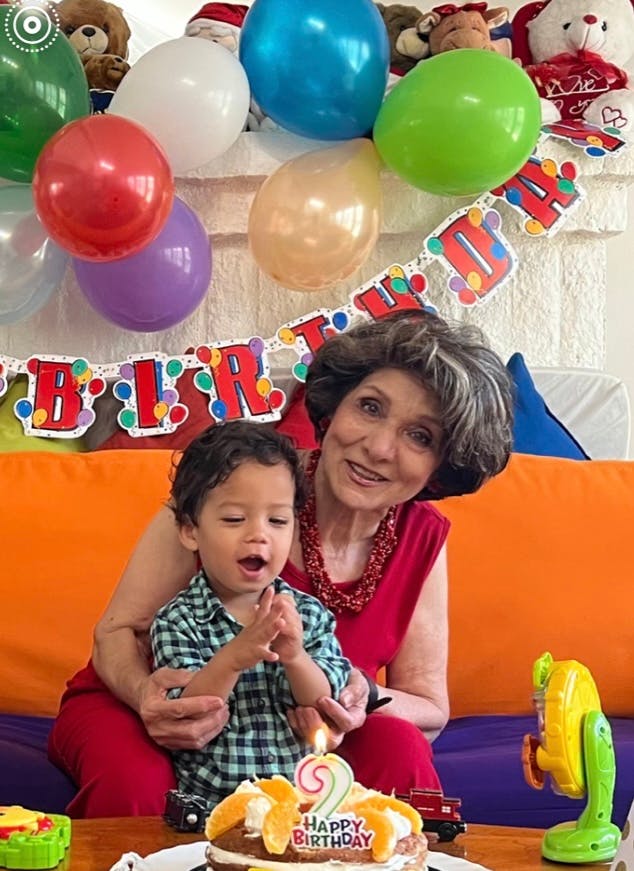Person holding a child in front of a birthday cake with balloons and balloons