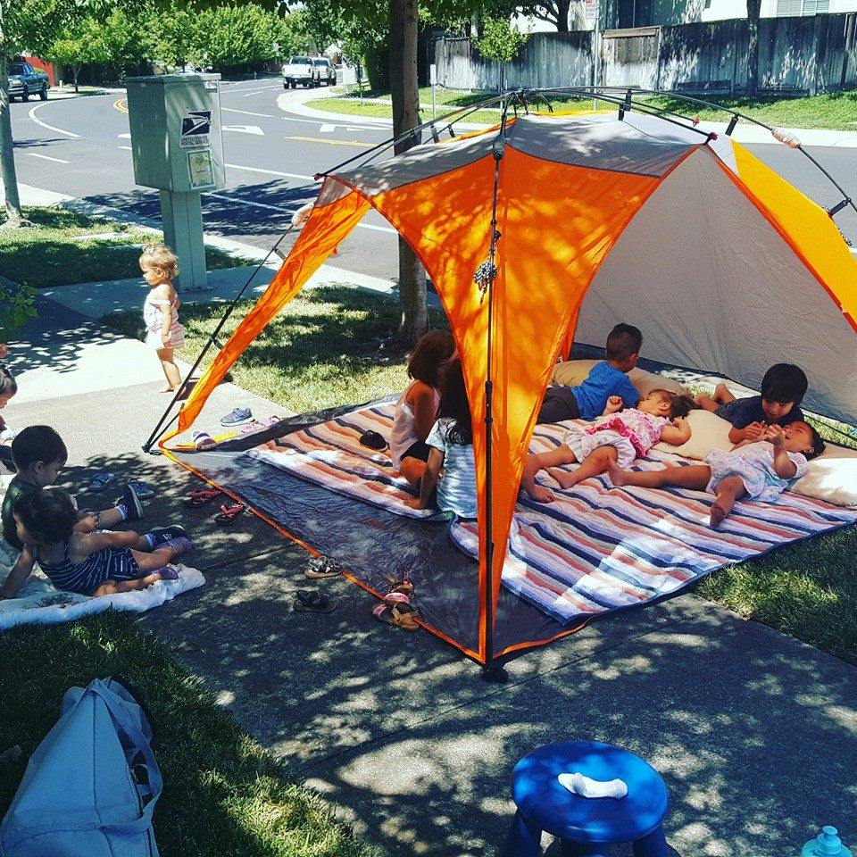 Children resting inside and outside an orange tent