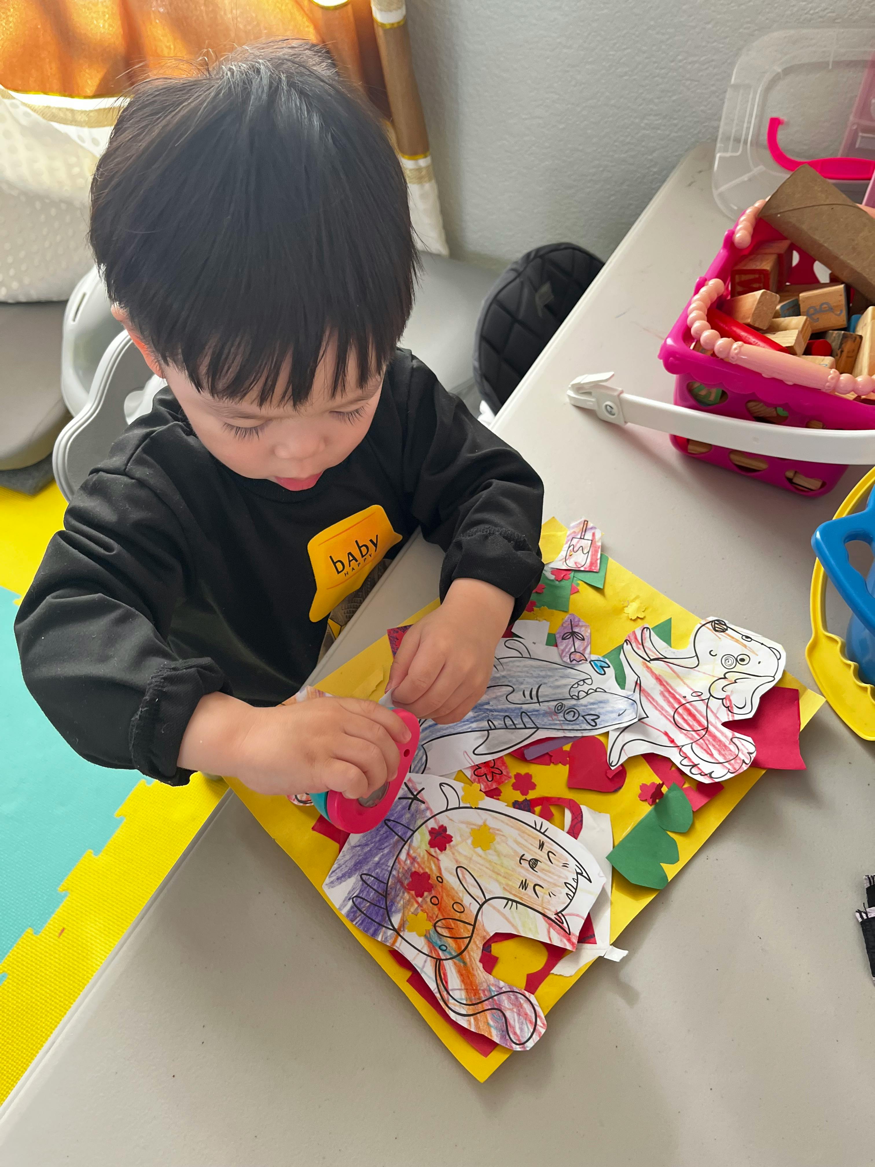 Child playing with paper cutouts and drawings on a yellow mat