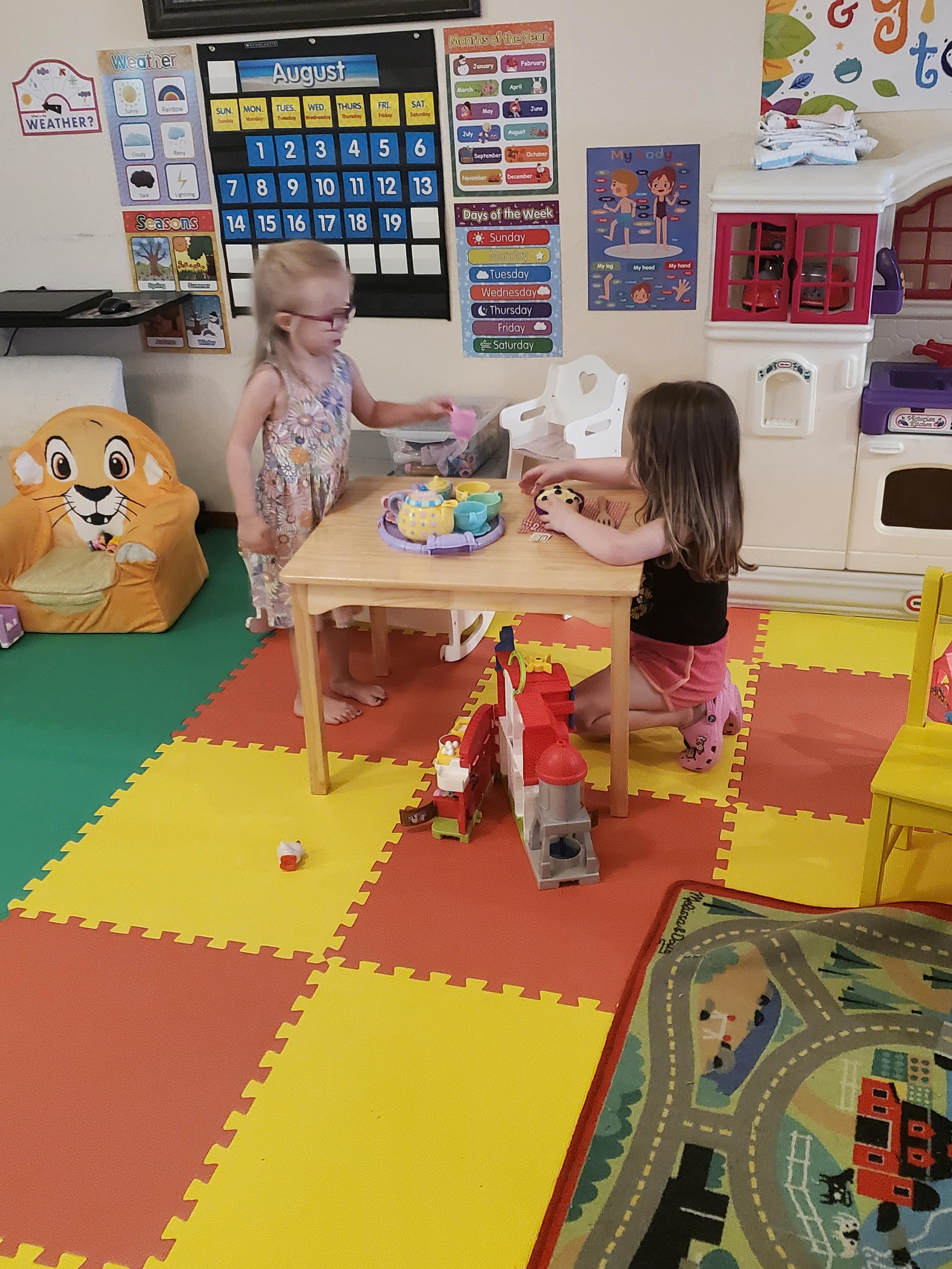 Two children playing with toys at a small table in a classroom