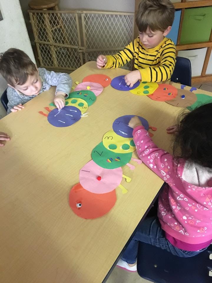 Three children playing with colorful caterpillar cutouts on a table