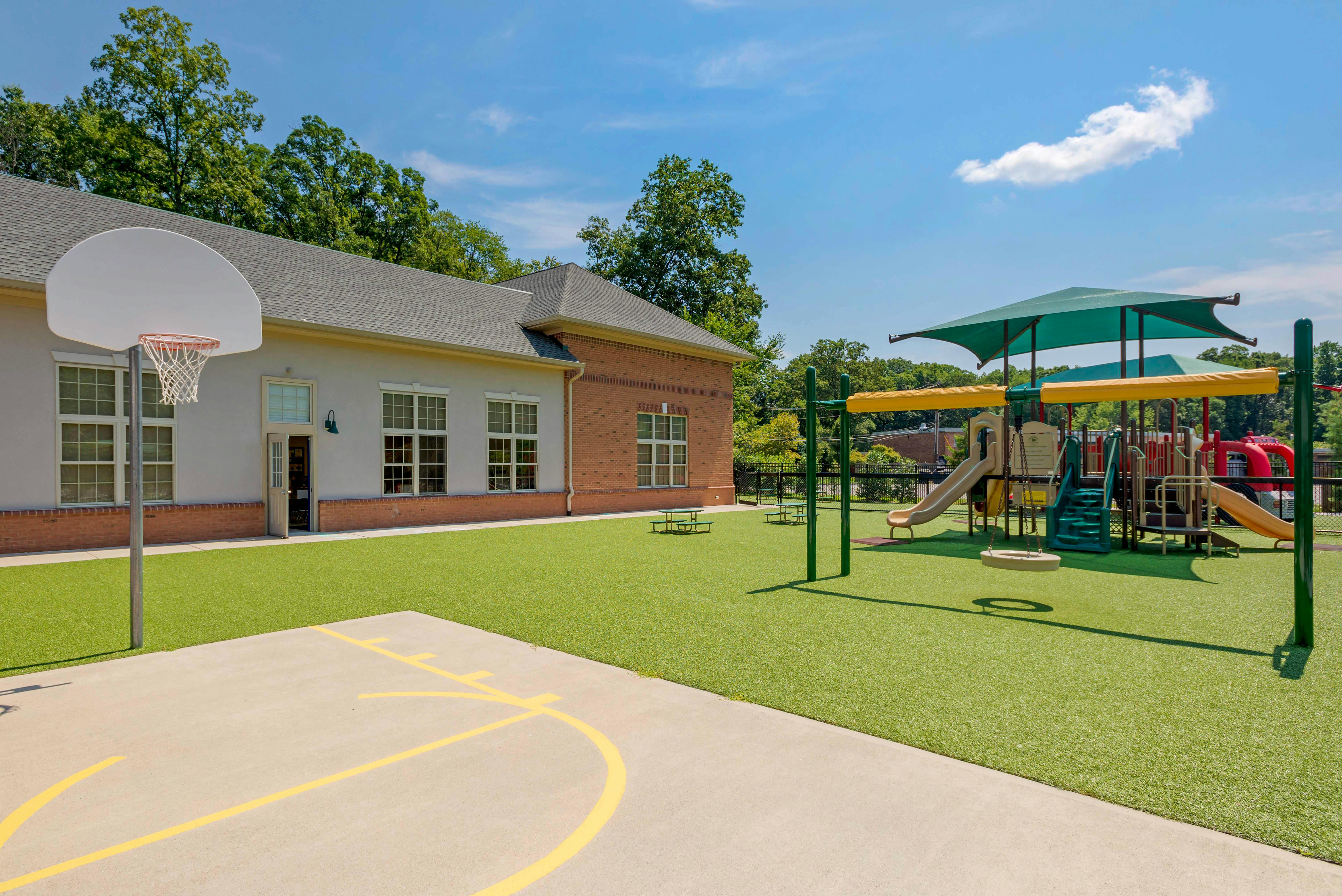 Basketball hoop on a court next to a building and playground with artificial turf