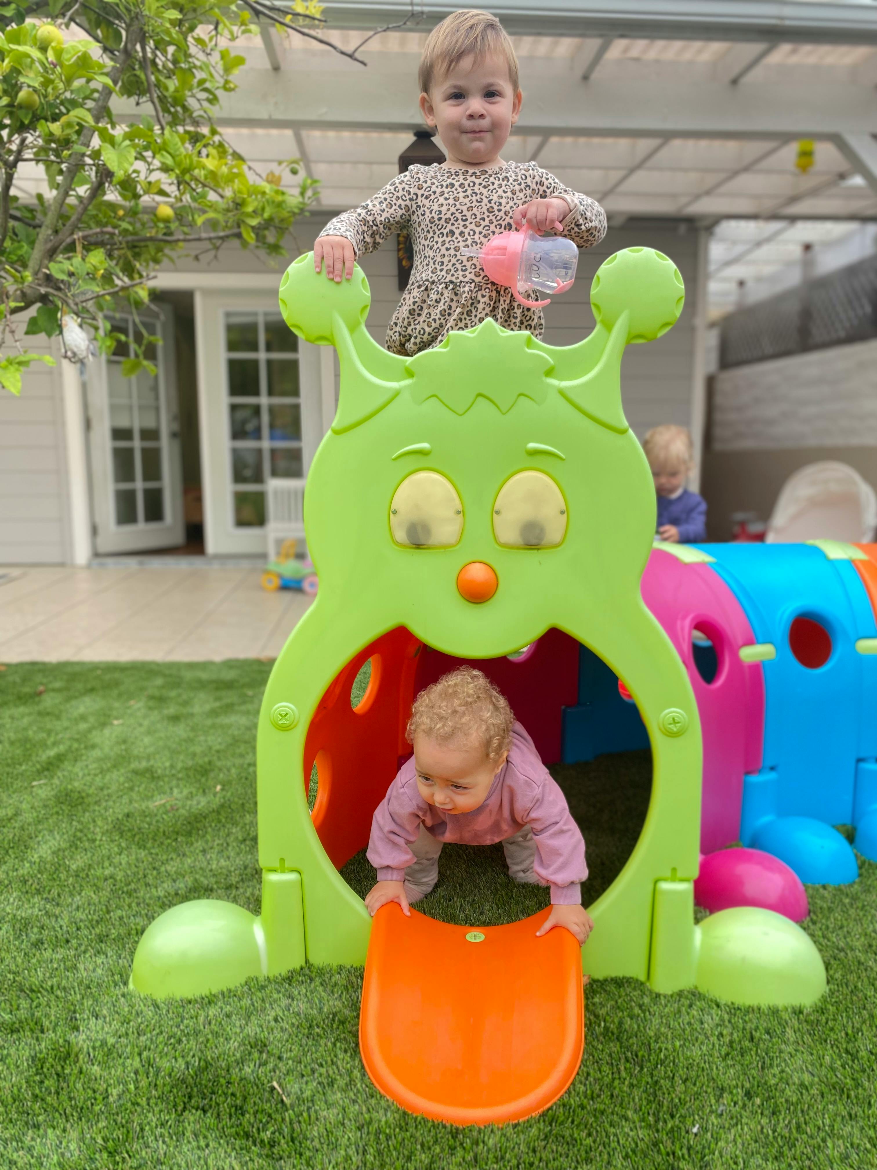 Child standing on top of a green play structure, another child crawling out