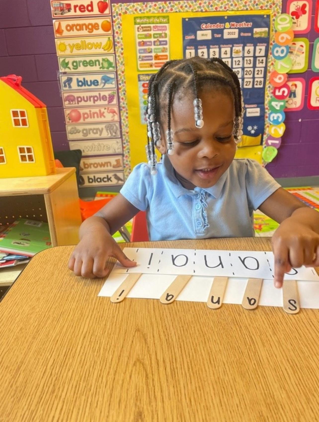 Child at a desk manipulating a word puzzle with popsicle sticks in a classroom
