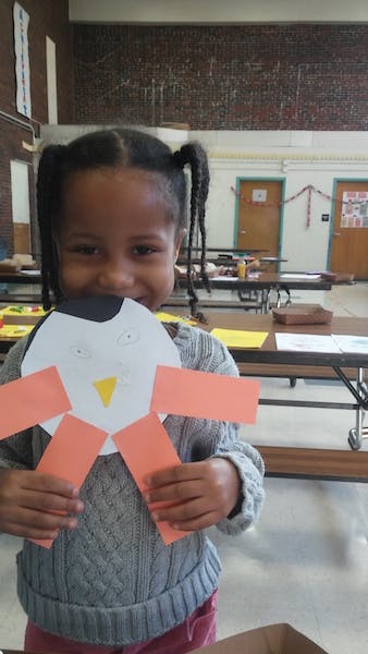 Child holding up a paper craft of a penguin