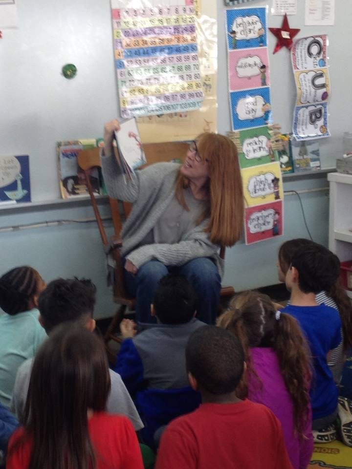 Person reading a book to a group of children in a classroom