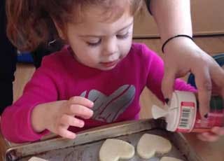Child decorating heart-shaped cookies on a baking sheet