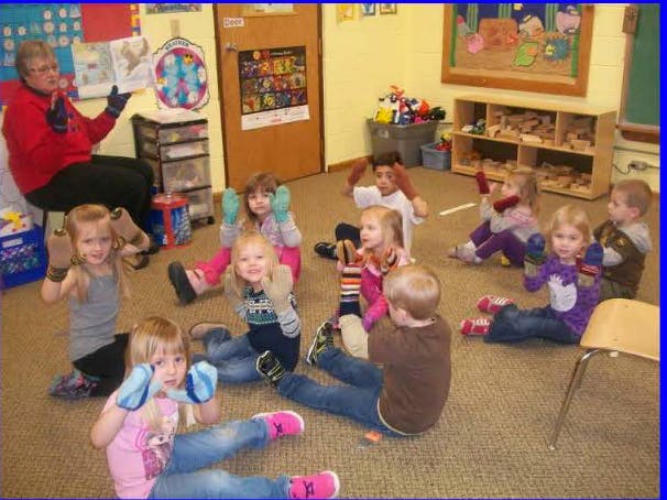 Person and children sitting on floor wearing mittens in a classroom