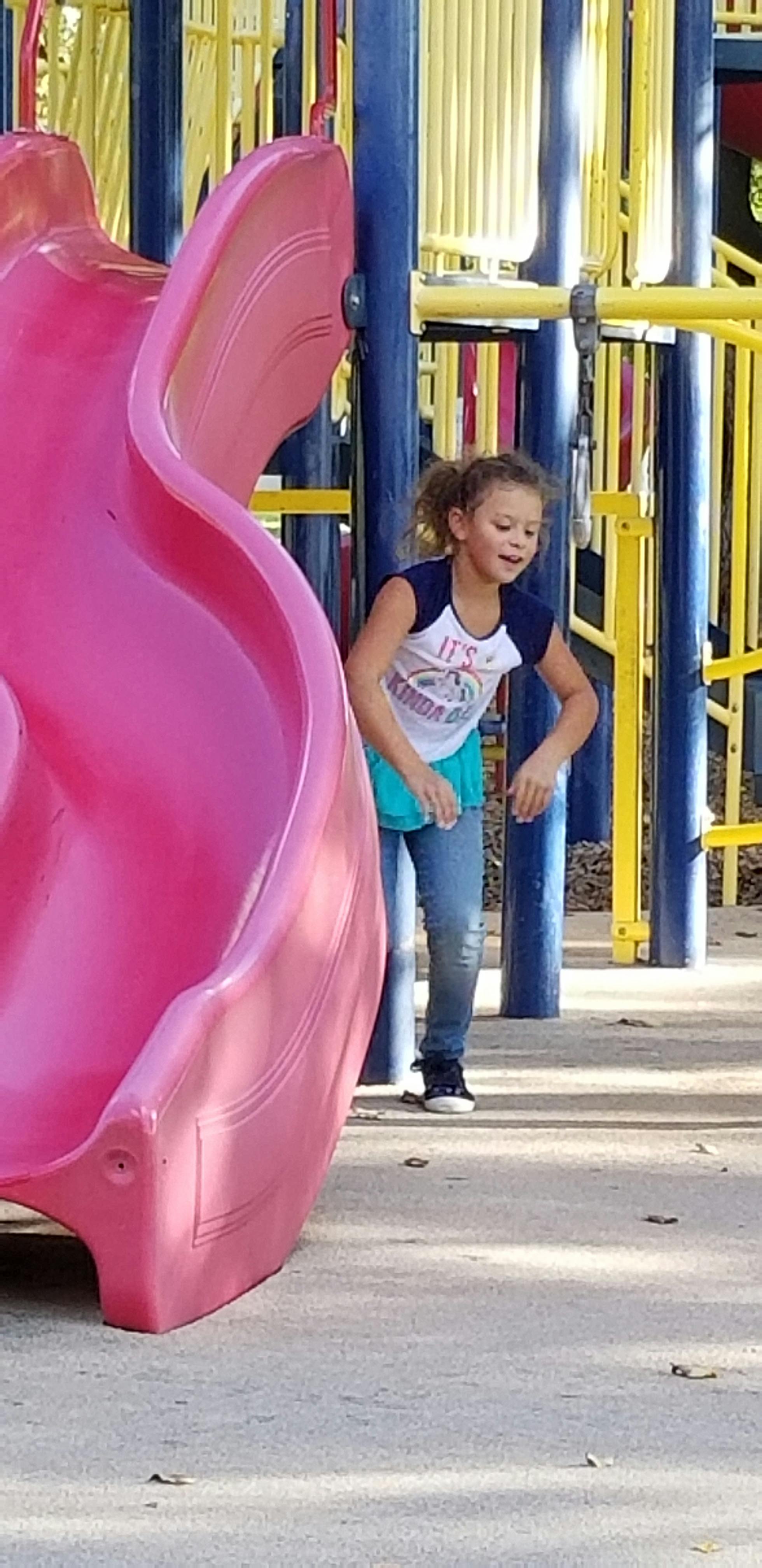 Child standing next to a pink slide on a playground