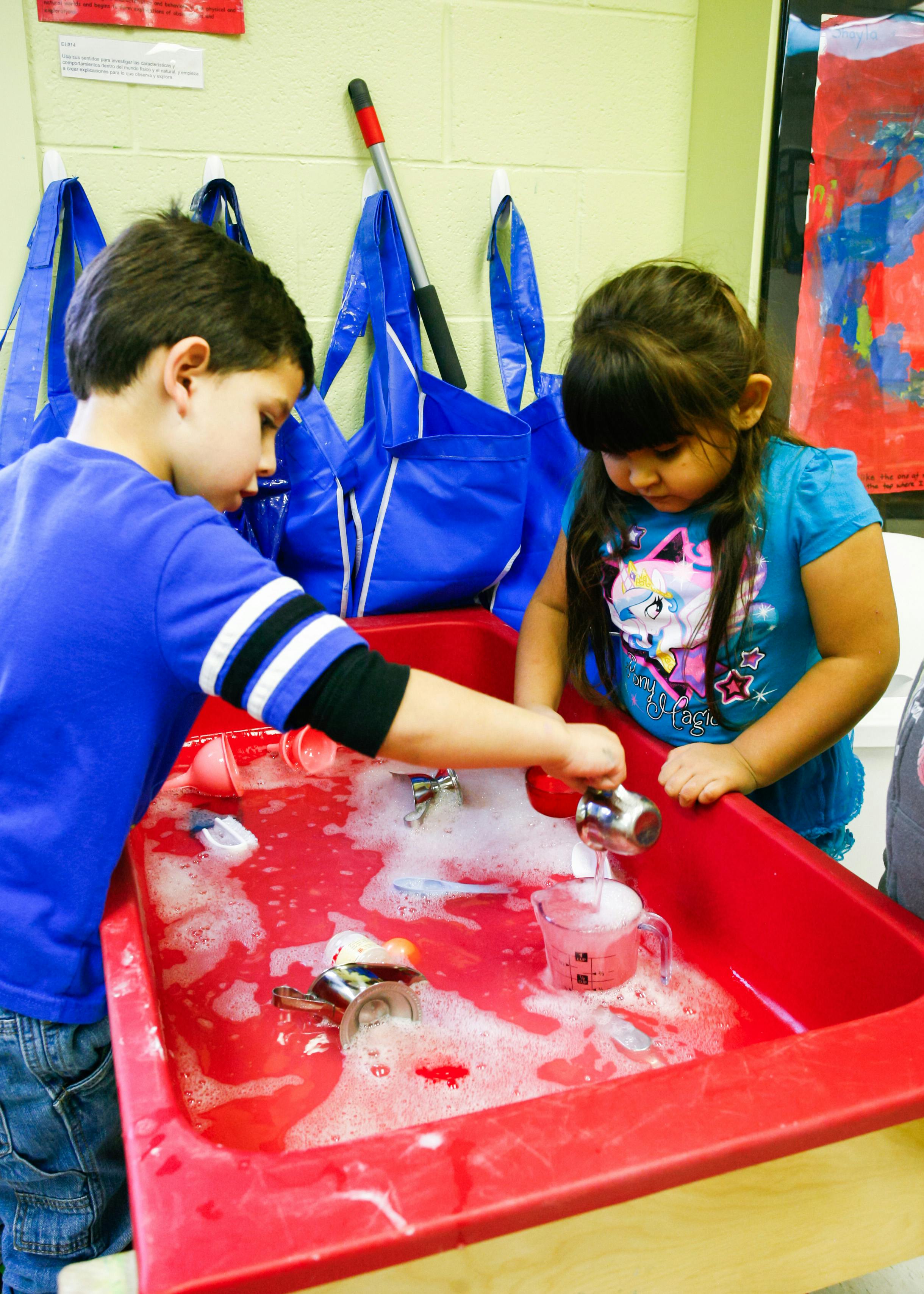 Two children playing with water and bubbles in a red bin