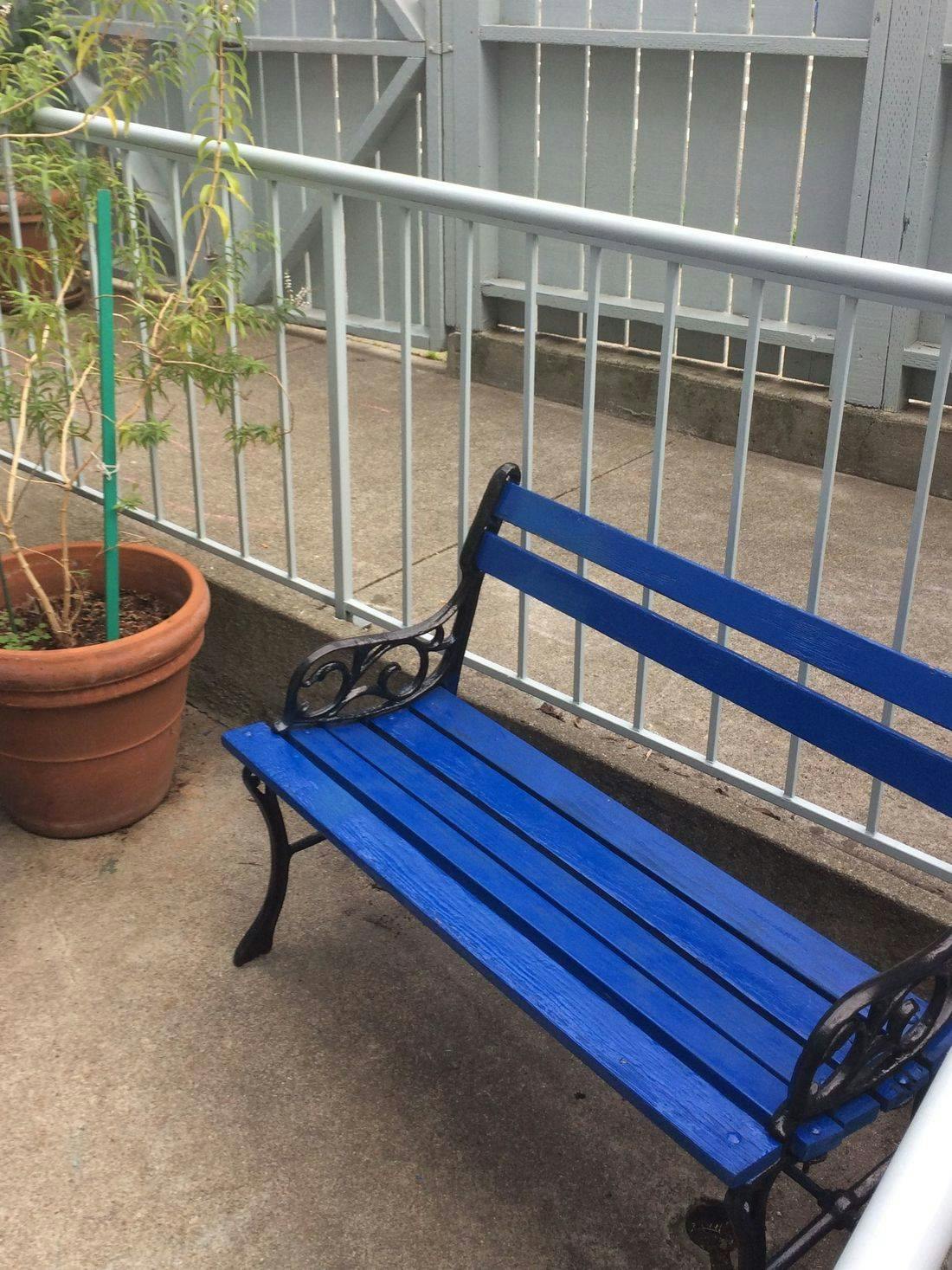 Blue park bench next to a potted plant and metal fence
