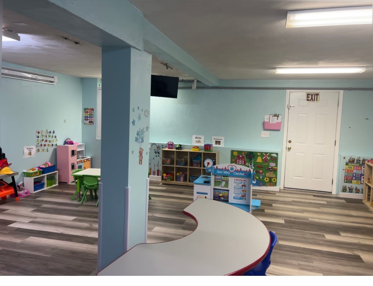 Empty classroom with small tables and chairs, shelves, and an exit door
