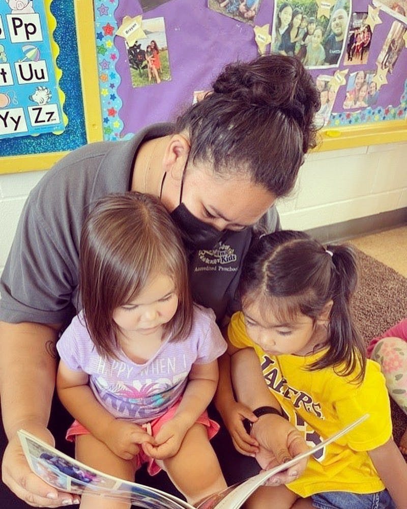 Person wearing a mask reading a book to two children