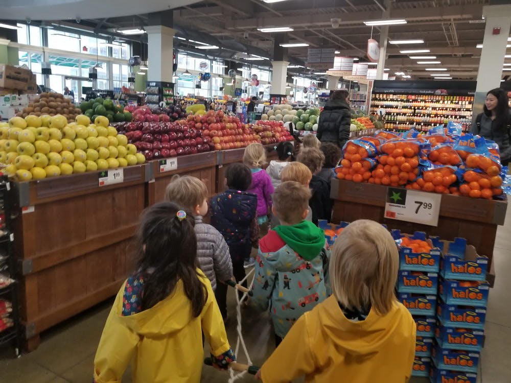 Children walking in a line past fruit displays in a grocery store