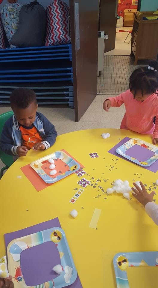 Two children at a yellow table doing crafts with cotton balls and paper