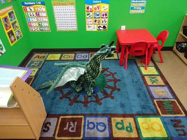 Stuffed dragon on a rug with alphabet letters in a classroom