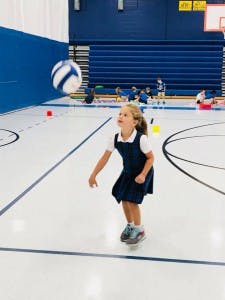 Child in uniform playing with a volleyball in a gymnasium