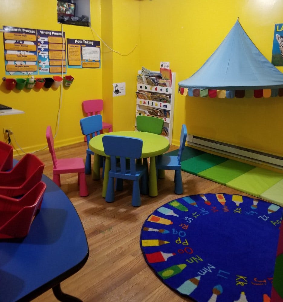 Children's classroom with small tables and chairs, a play tent, and a colorful rug