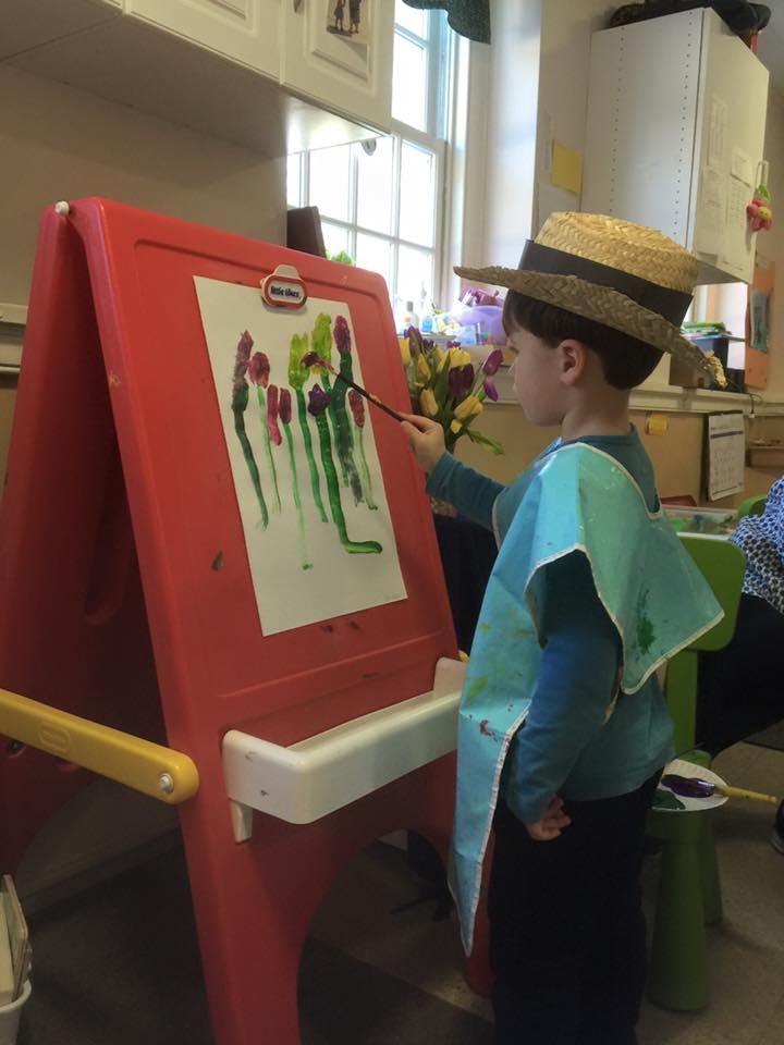 Child in a straw hat painting on an easel