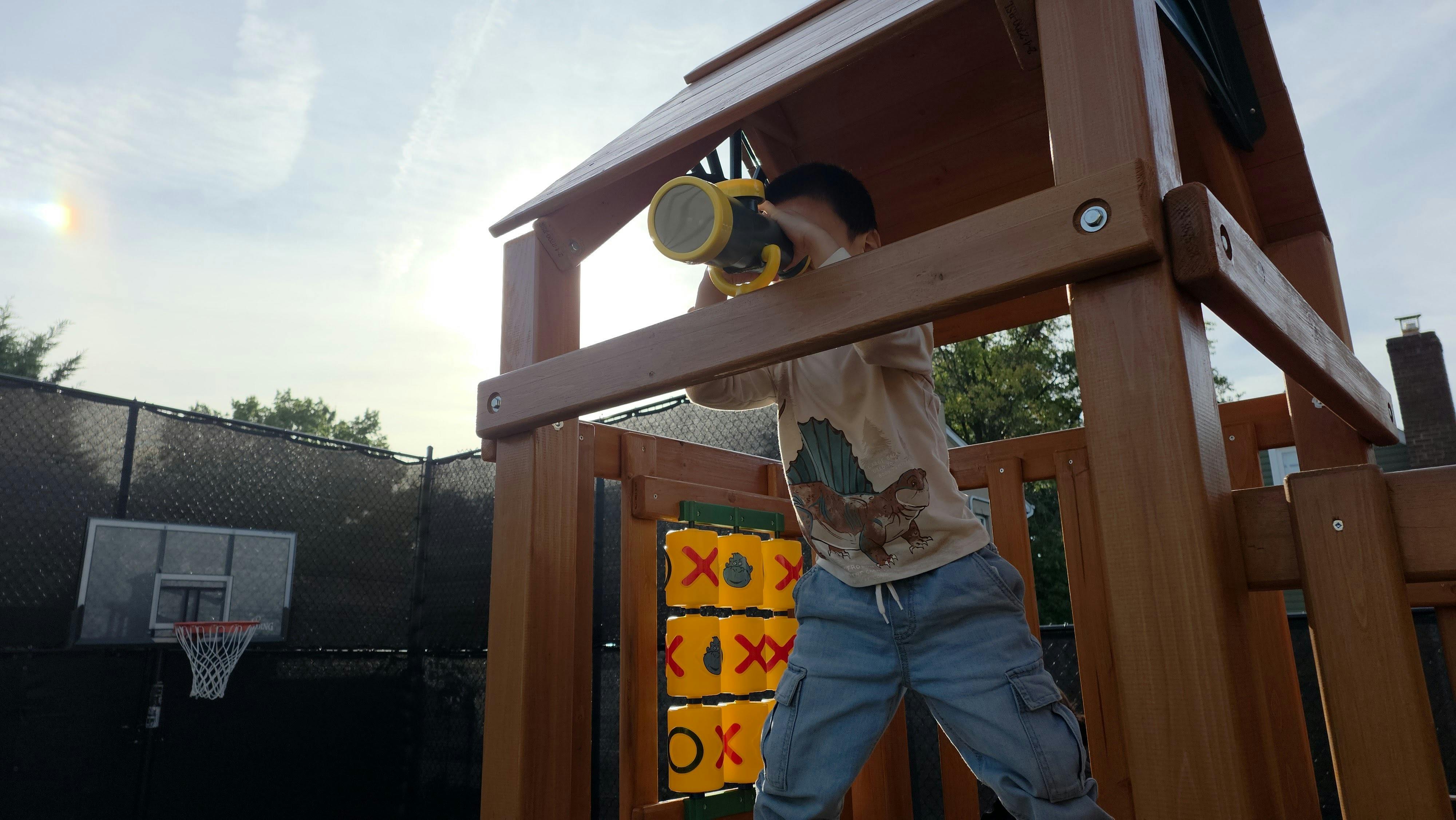Child looking through a telescope on a wooden playground structure