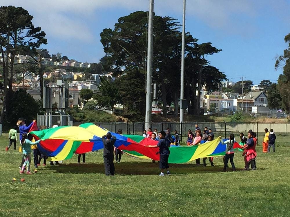 People playing with a large colorful parachute on a grassy field