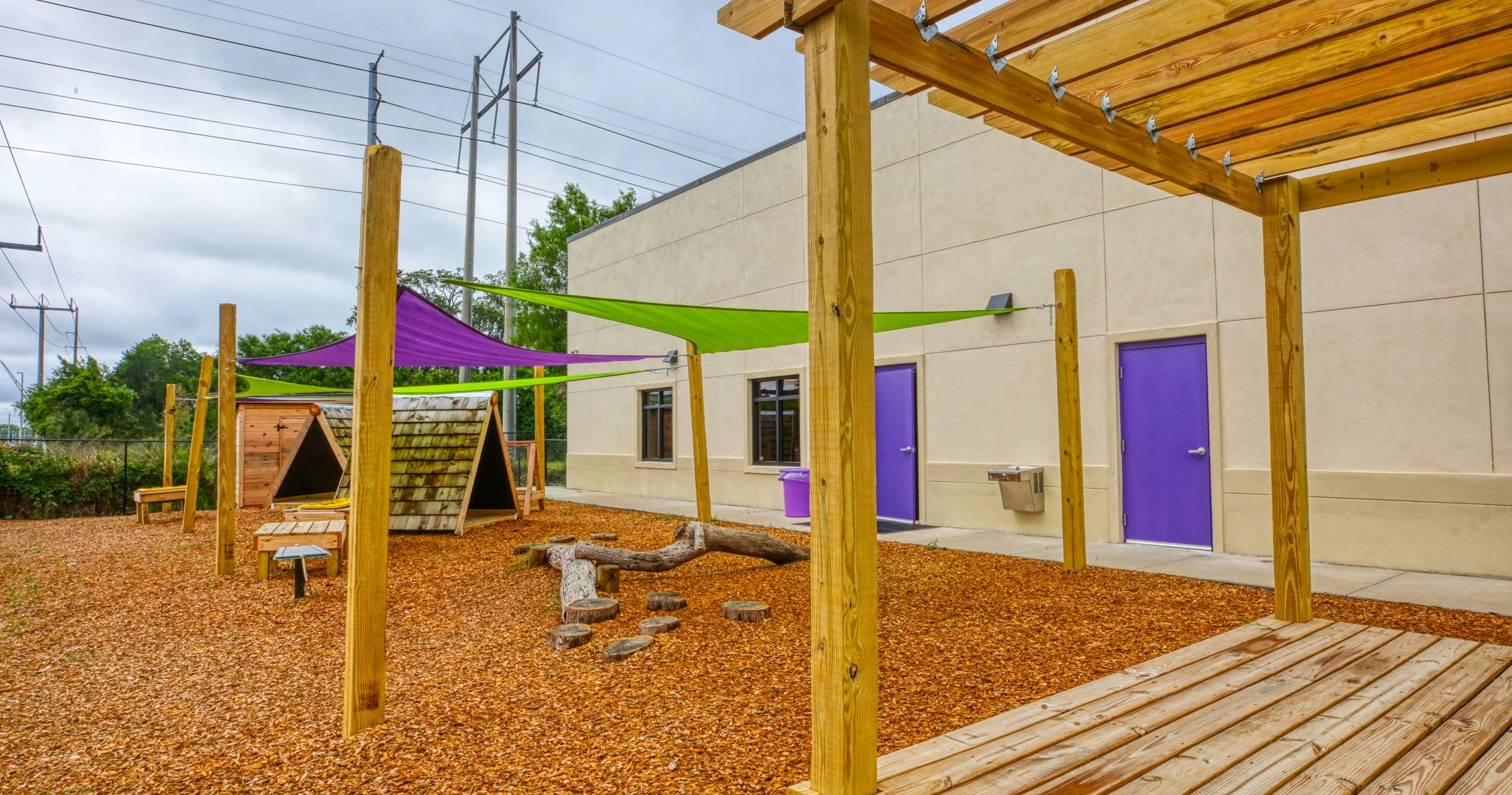 Outdoor play area with wood chips, shade sails, and play structures