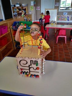 Child playing with a wooden activity cube in a classroom