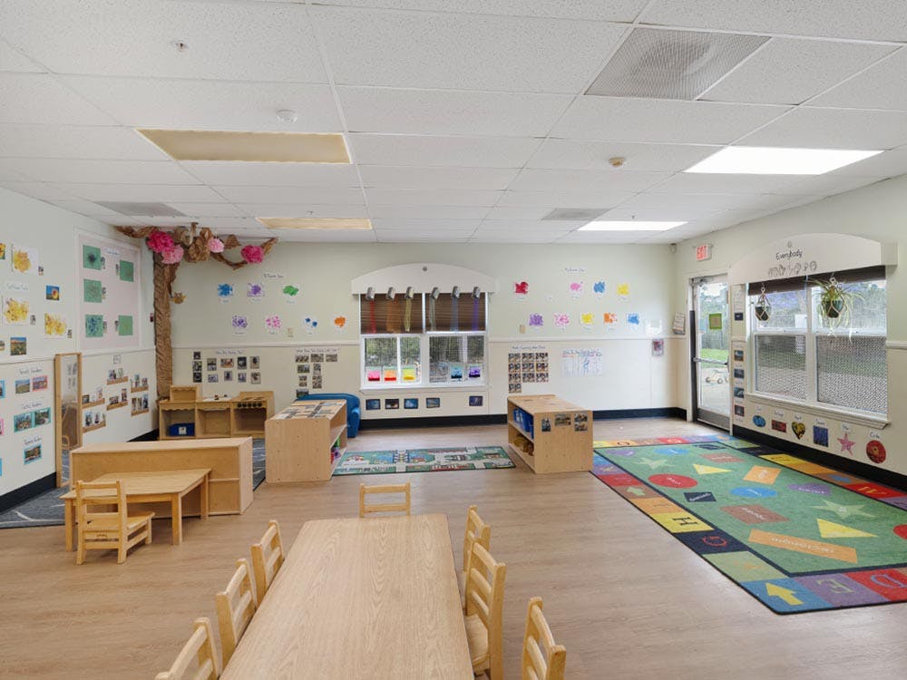 Empty classroom with small wooden tables and chairs, colorful rug