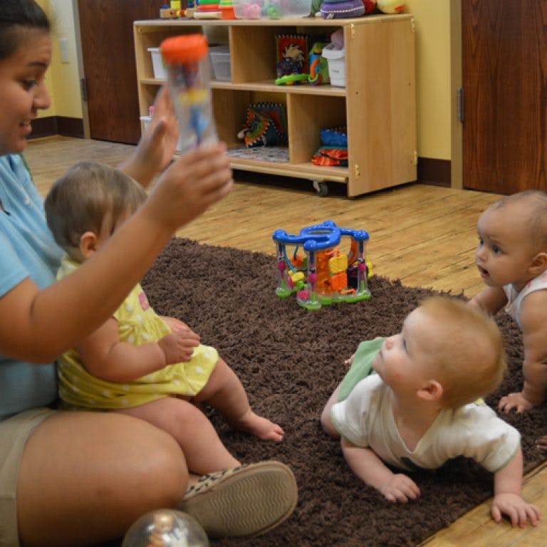 Person holding a toy for three children on a rug