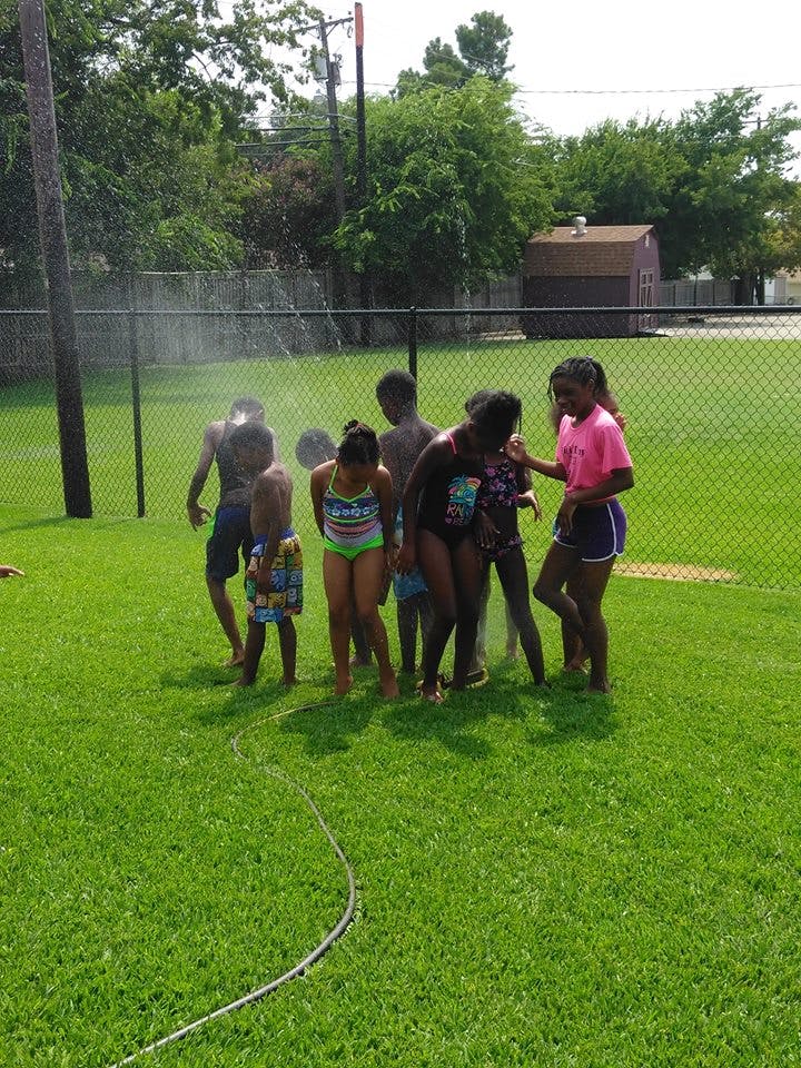 Children playing in water from a sprinkler on a grassy field