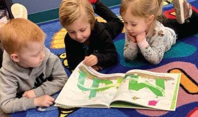 Three children lying on a rug looking at an open book
