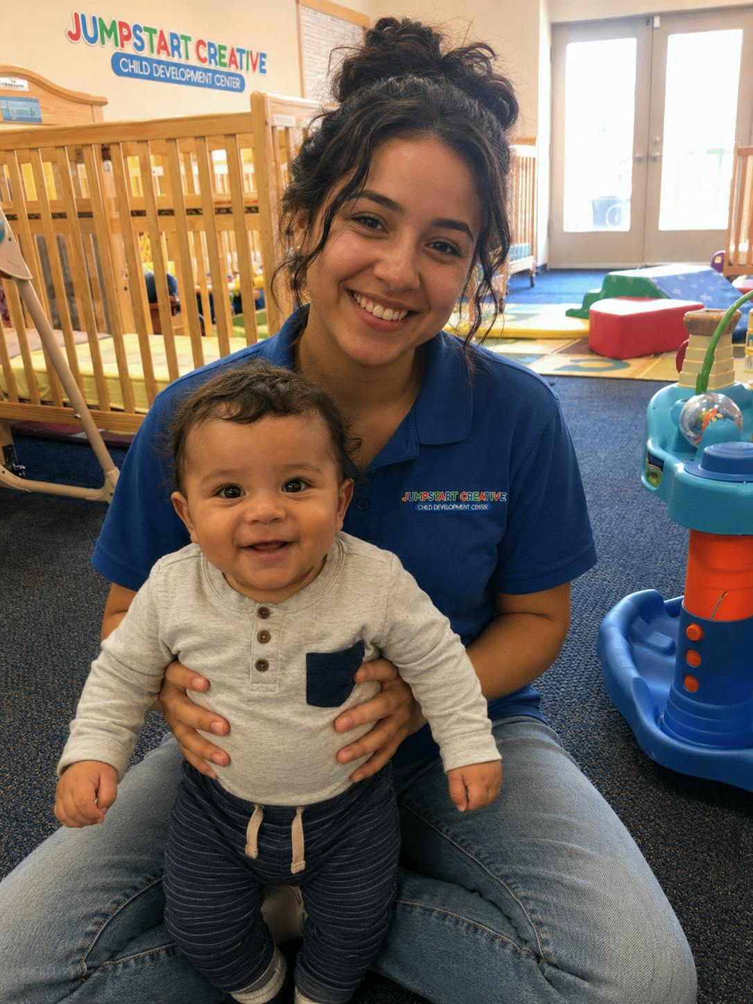 A person sitting on the floor holding a smiling baby in a childcare center