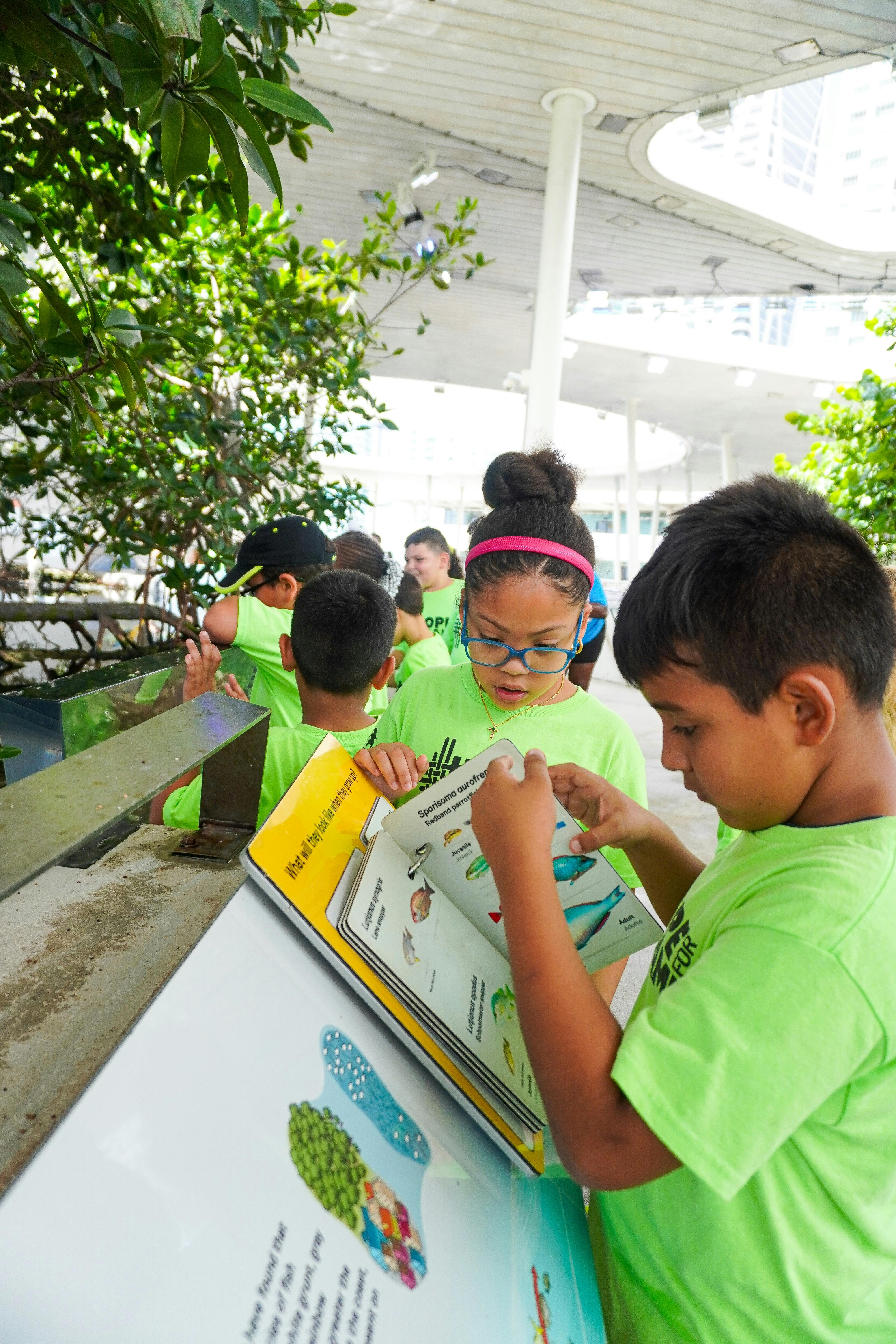 Group of children in matching green shirts reading an informational fish sign