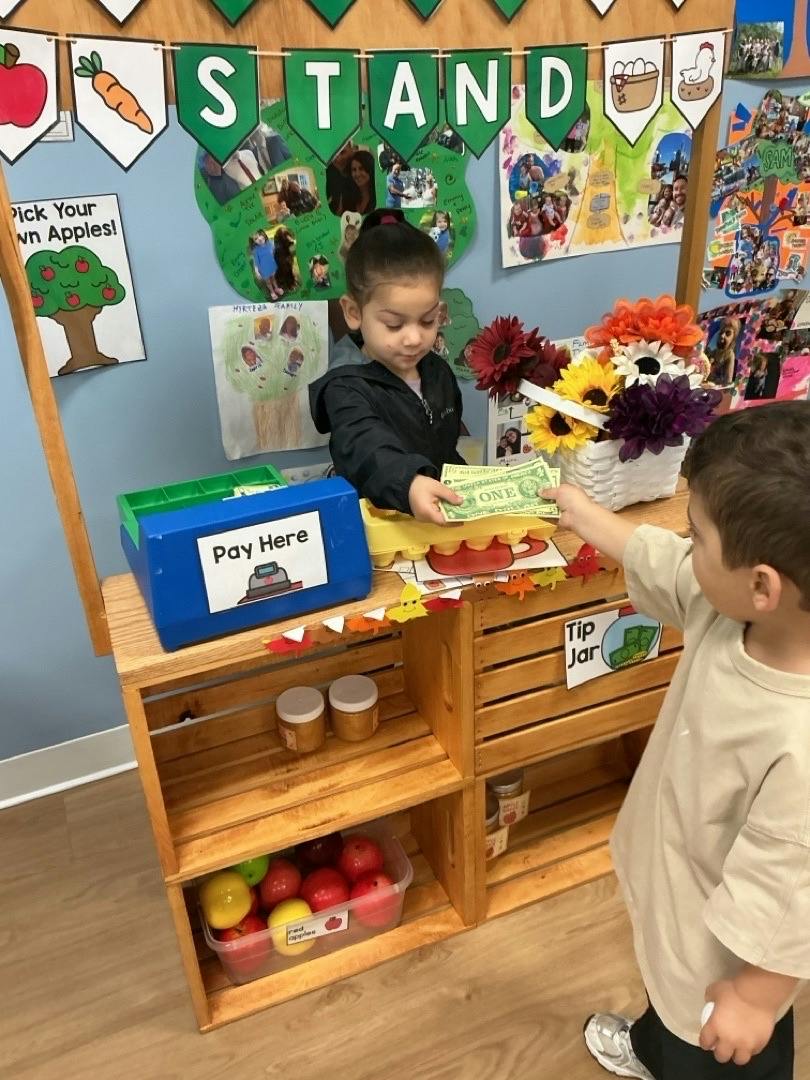Two children playing store with play money at a wooden stand