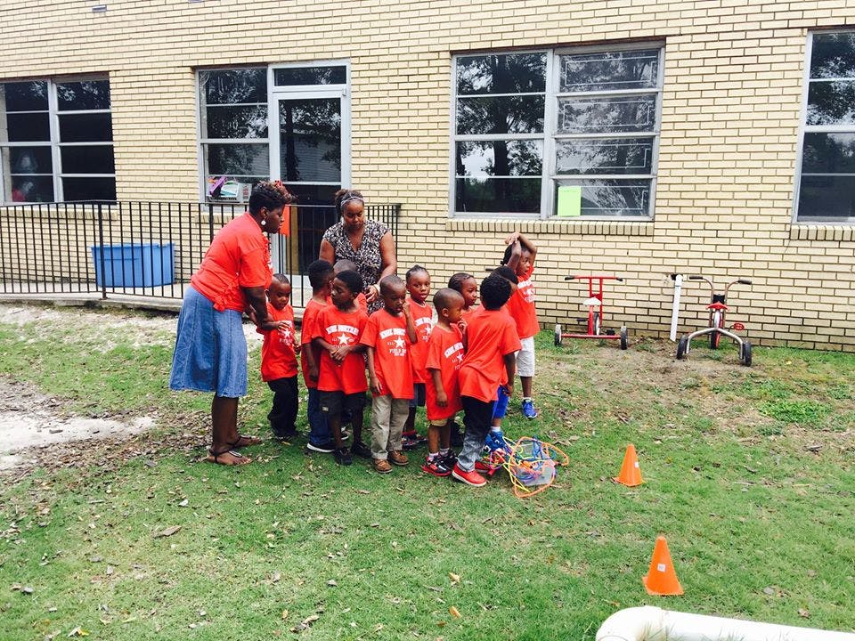 Two adults with a group of children in red shirts on grass