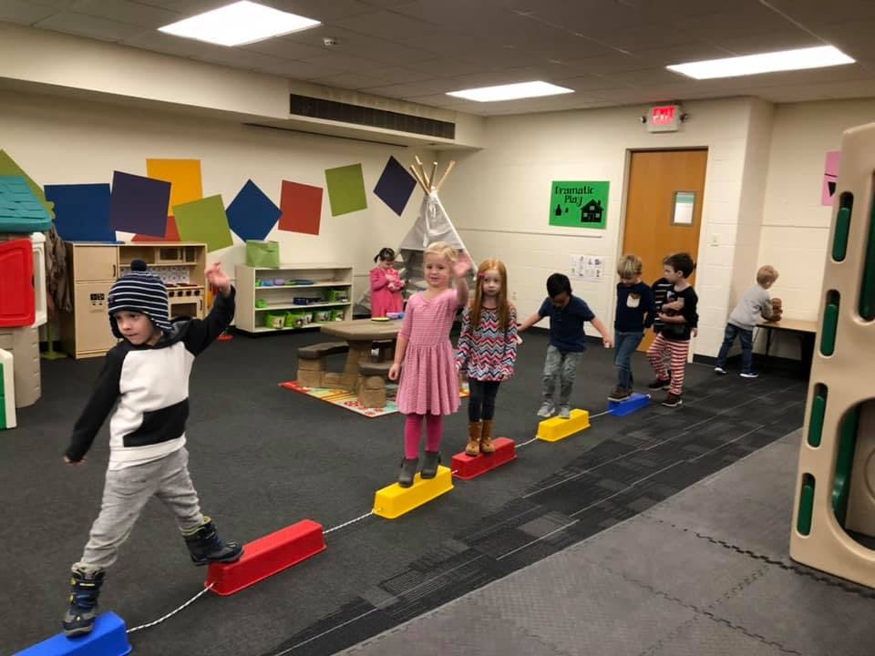 Children walking on a balance beam in a classroom