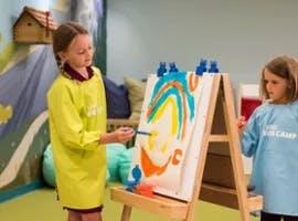 Child painting on an easel with another child standing nearby