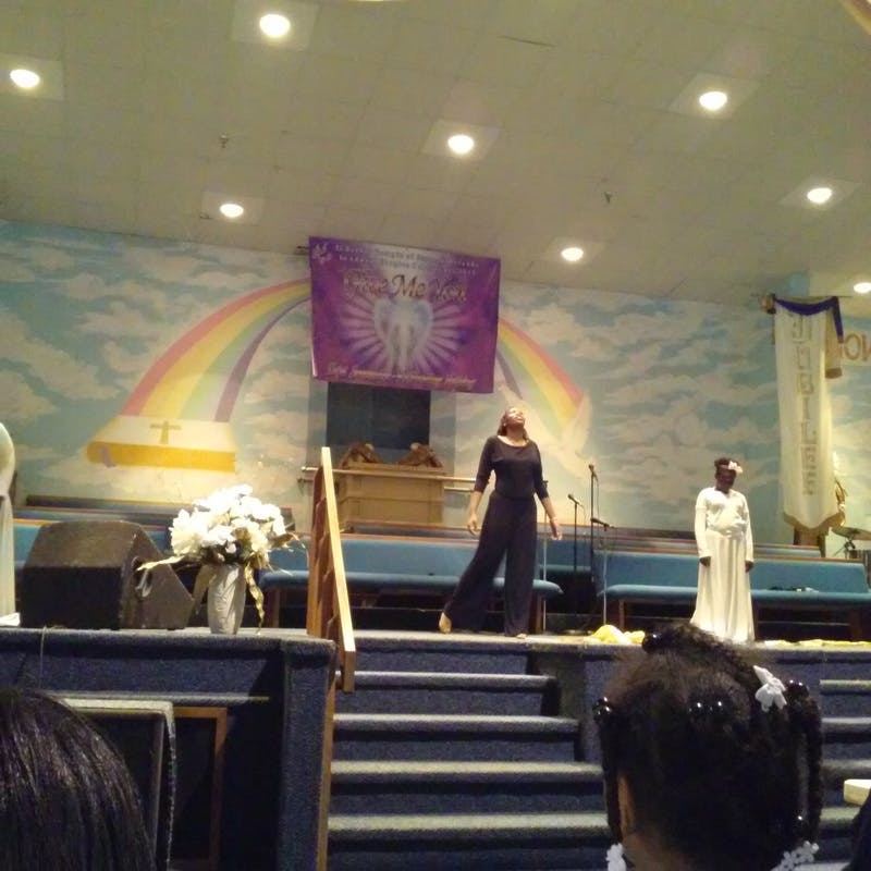 Person in black standing on a stage with a rainbow mural
