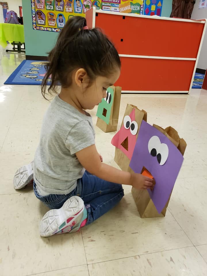 Child playing with paper bag puppets in a classroom