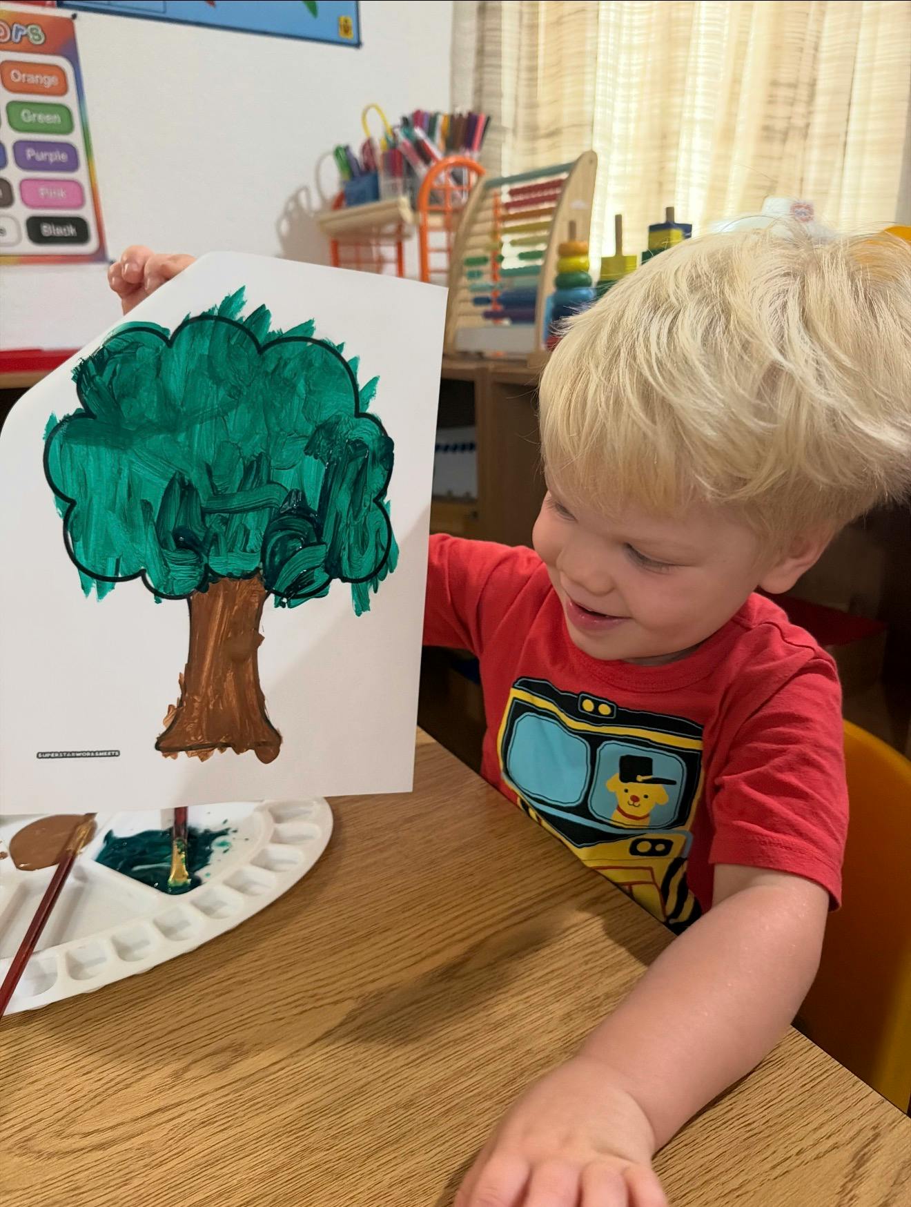 Child holding up a paper with a painted tree