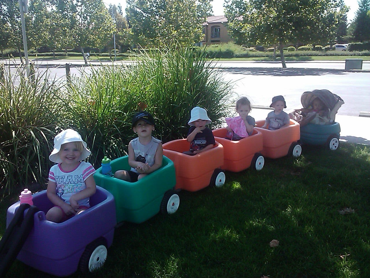 Children sitting in colorful toy train cars on grass